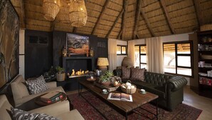 A cozy living room with a fireplace, leather sofa, and a large window with curtains. -  Kwessi Dunes (Sesriem)