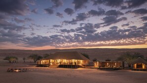 A desert resort with thatched-roof structures, outdoor seating, and a view of the desert landscape. -  Kwessi Dunes (Sesriem)