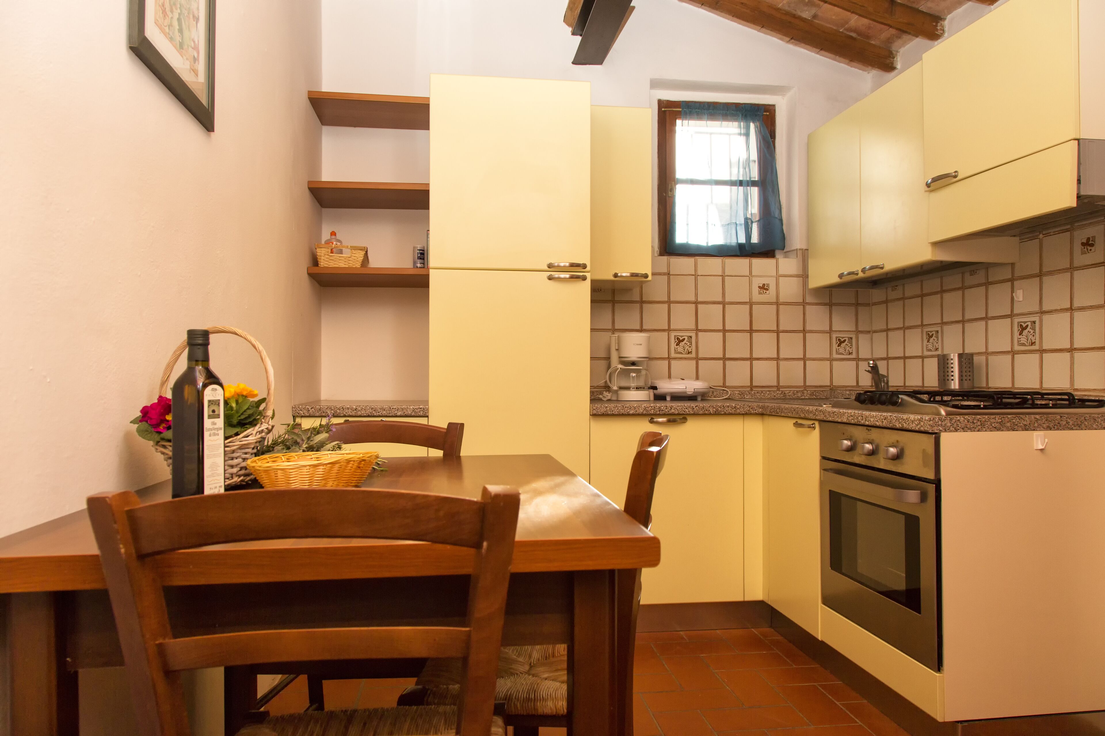 Una cocina compacta con una mesa y sillas, horno empotrado y una ventana con cortina.