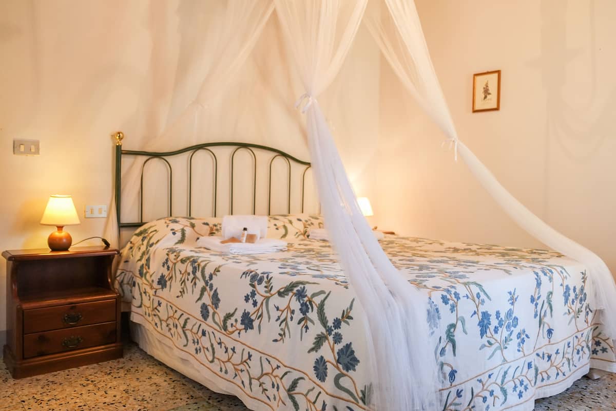 A bed with a canopy, a nightstand with a lamp, and a wall-mounted light switch.