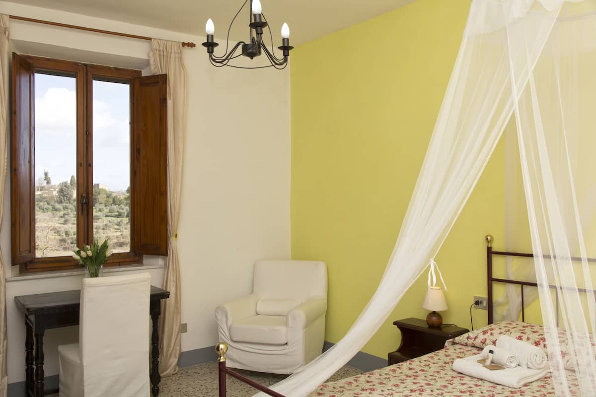 A bedroom with a bed, a chair, a desk, and a window with curtains.