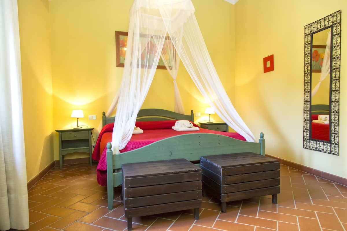 A room with a bed under a canopy, two bedside tables with lamps, a mirror on the wall, and a red pillow on the bed.