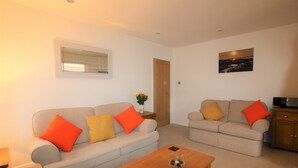 Ein Wohnzimmer mit zwei Sofas, einem Couchtisch, einem Fernseher und einer Tür.