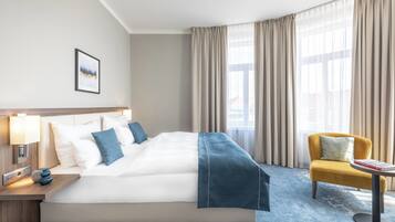 A hotel room with a large bed, a bedside table with a lamp, a chair, and a window with curtains.