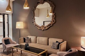 A modern living room with a beige sofa, two armchairs, a glass coffee table, and a large ornate mirror.