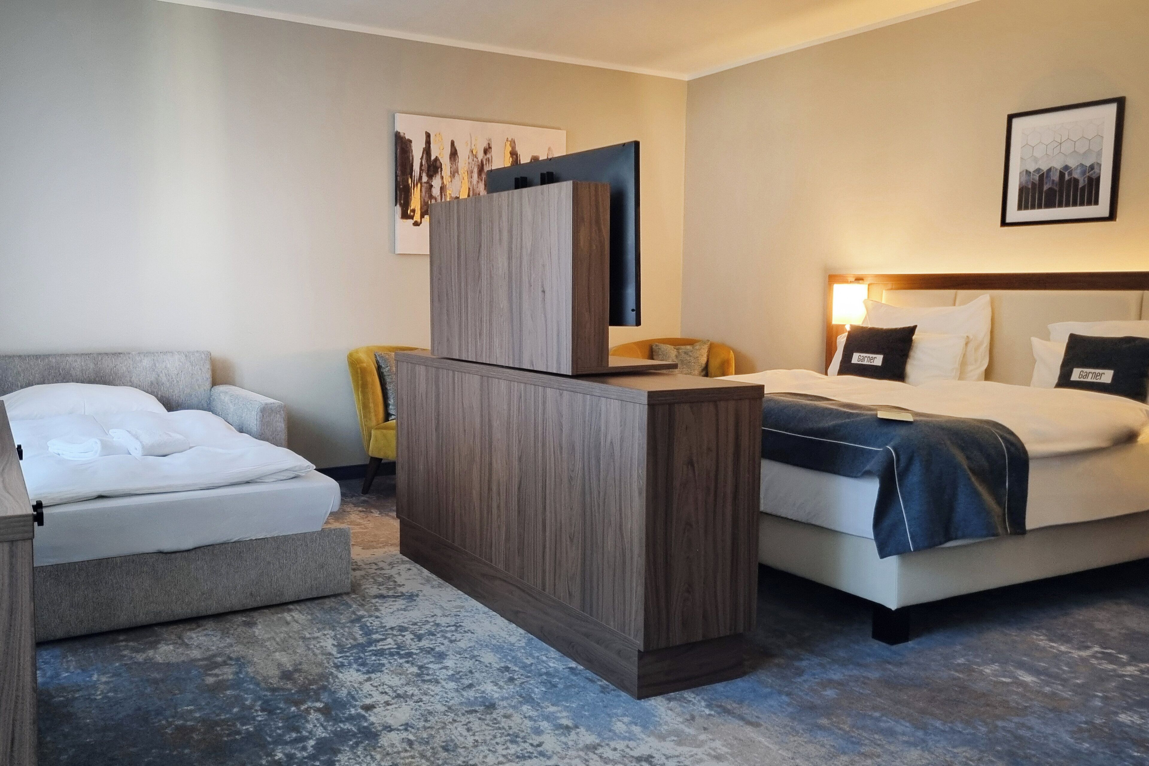 Ein Hotelzimmer mit einem Bett, einem Schreibtisch und einem Sessel. Es gibt zwei Betten, einen Schreibtisch mit einem Computer und einen Sessel.