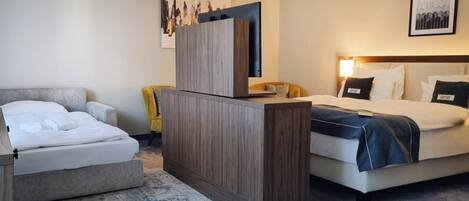 Ein Hotelzimmer mit einem Bett, einem Schreibtisch und einem Sessel. Es gibt zwei Betten, einen Schreibtisch mit einem Computer und einen Sessel.