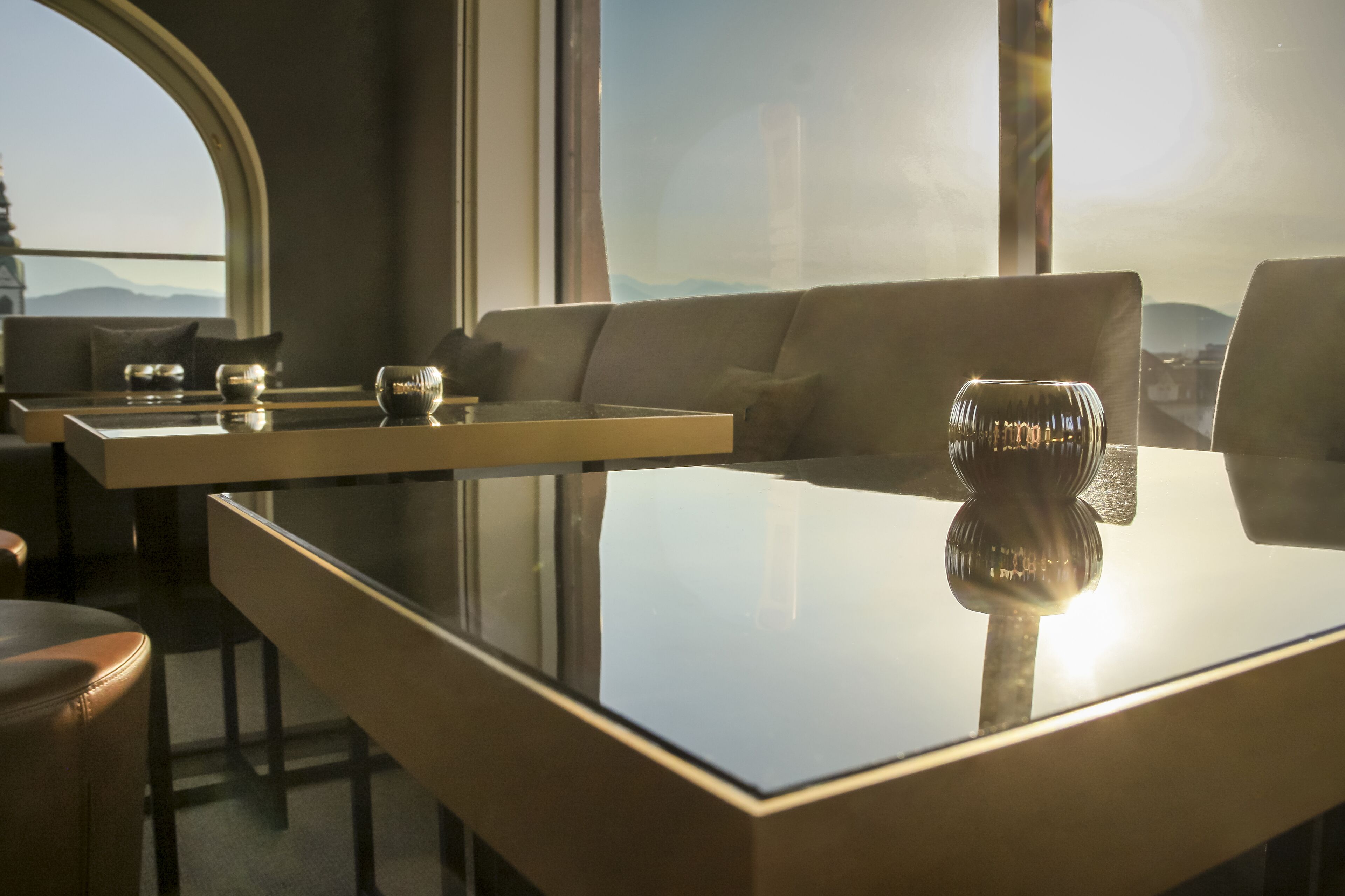 A modern interior with a glass-top table, leather sofa, and a view of the mountains through a large window.