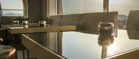 A modern interior with a glass-top table, leather sofa, and a view of the mountains through a large window.