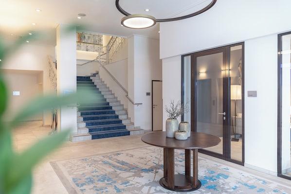 A modern interior with a staircase, a round table with vases, and a glass door labeled "Lounge".