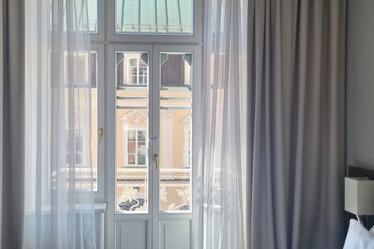 Ein Zimmer mit großem Fenster, durchsichtigen Vorhängen und Blick auf ein Gebäude.
