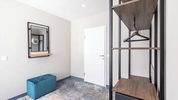 A room with a white door, a blue bench, a mirror with a black frame, and a wooden shelf with a hanger.