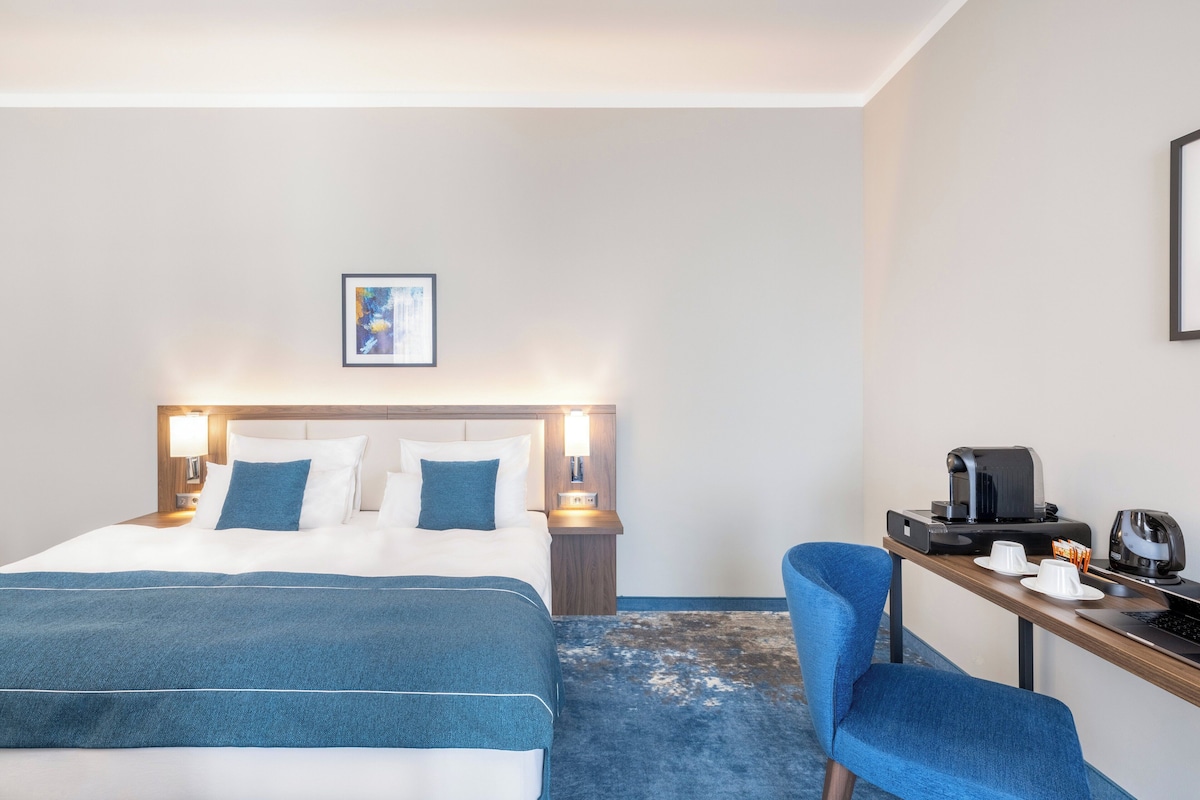 Ein Hotelzimmer mit einem Bett, einem Schreibtisch mit Kaffeemaschine und einem Sessel.