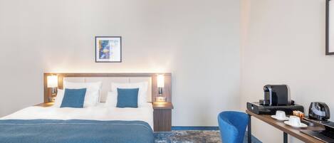 A hotel room with a bed, a desk with a coffee maker, and a chair.