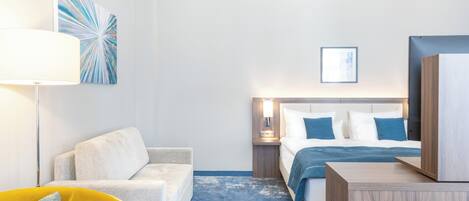 A modern hotel room with a bed, a sofa, a desk, and a lamp.