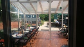 Een restaurant met een glazen overkapping, houten vloeren en zichtbare buitenterrassen.