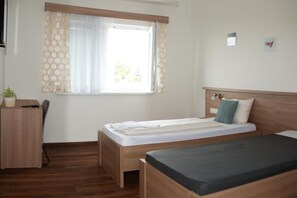Une chambre avec deux lits, un bureau et une fenêtre avec des rideaux.