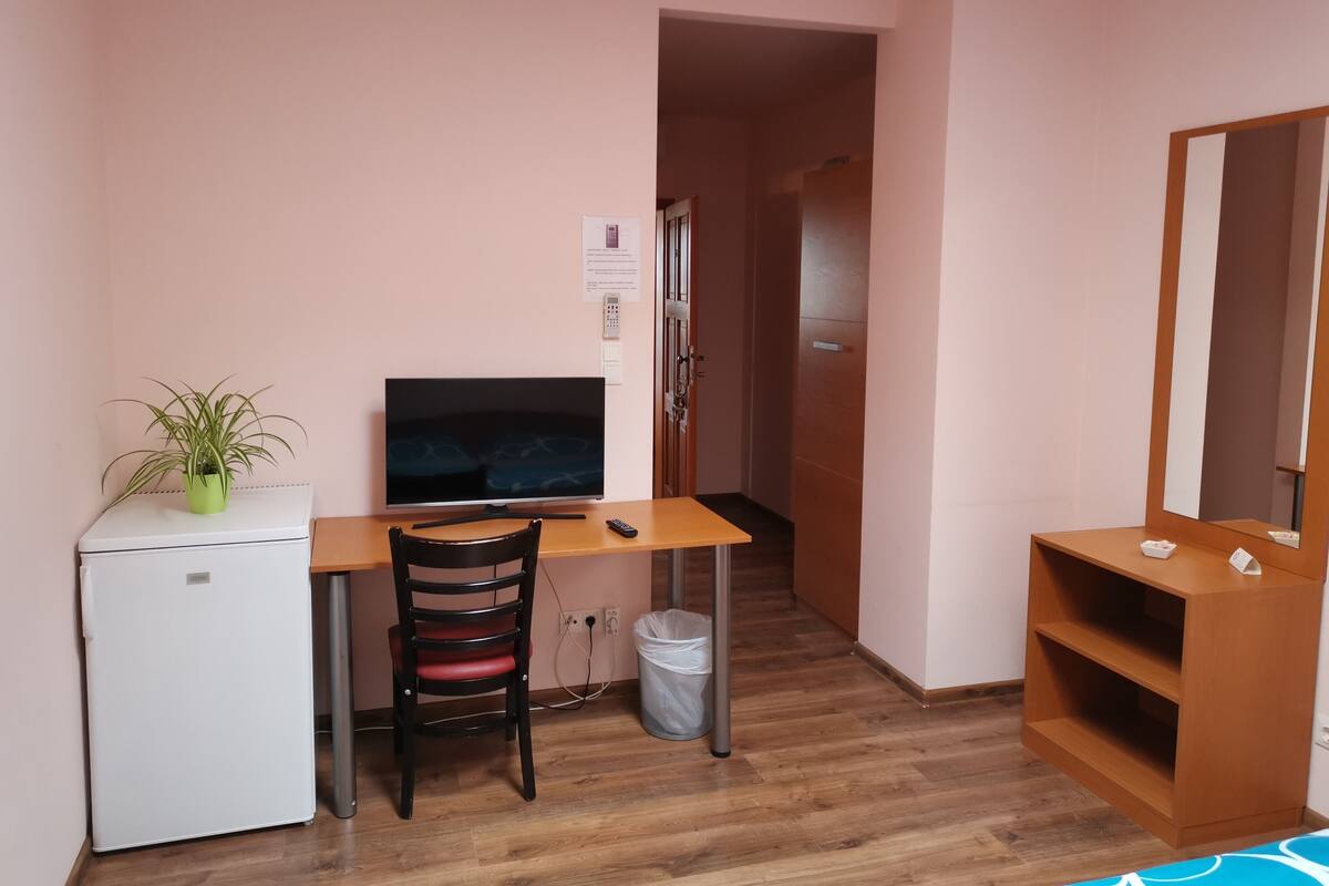 Une petite pièce comprenant un bureau, une chaise, un téléviseur et un petit réfrigérateur.