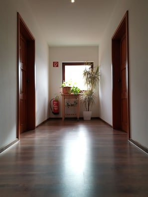 A hallway with wooden flooring, a fire extinguisher, and potted plants. - Hotel & Tenniscenter Khail (Maria Lanzendorf)