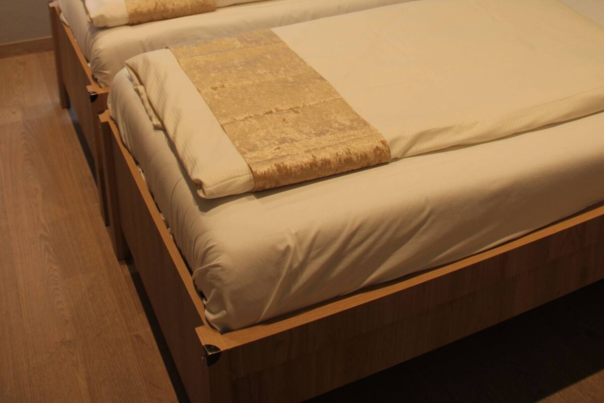 A bedroom with two single beds, a window with a blind, a radiator, and a wooden floor.