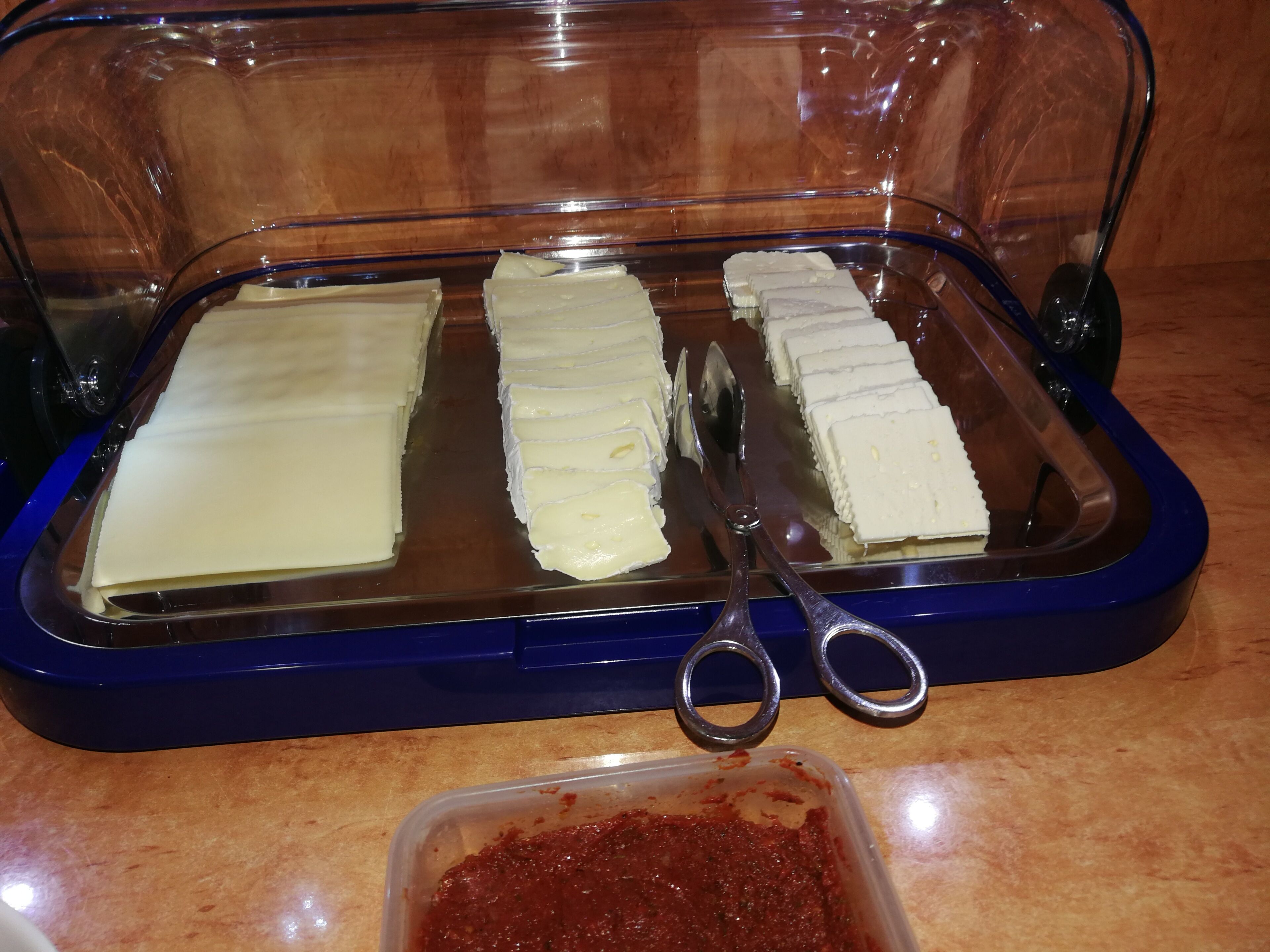 A food display with various cheese slices and a container of red sauce.
