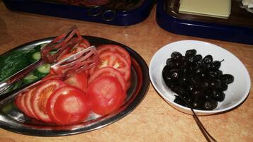 Ein Teller mit Tomaten- und Gurkenscheiben, eine Gabel, eine Schüssel schwarze Oliven und eine Platte mit Aufschnitt.