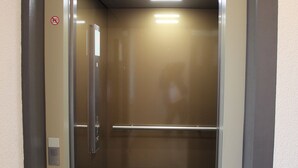 An elevator with a metallic interior, a handrail, and a no-smoking sign. - Hotel Bei Yasemin (Dorsten)