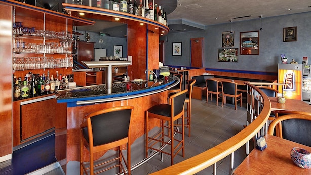 A bar area with wooden bar counters, stools, and a variety of bottles and glasses. - Hotel Bei Yasemin (Dorsten)
