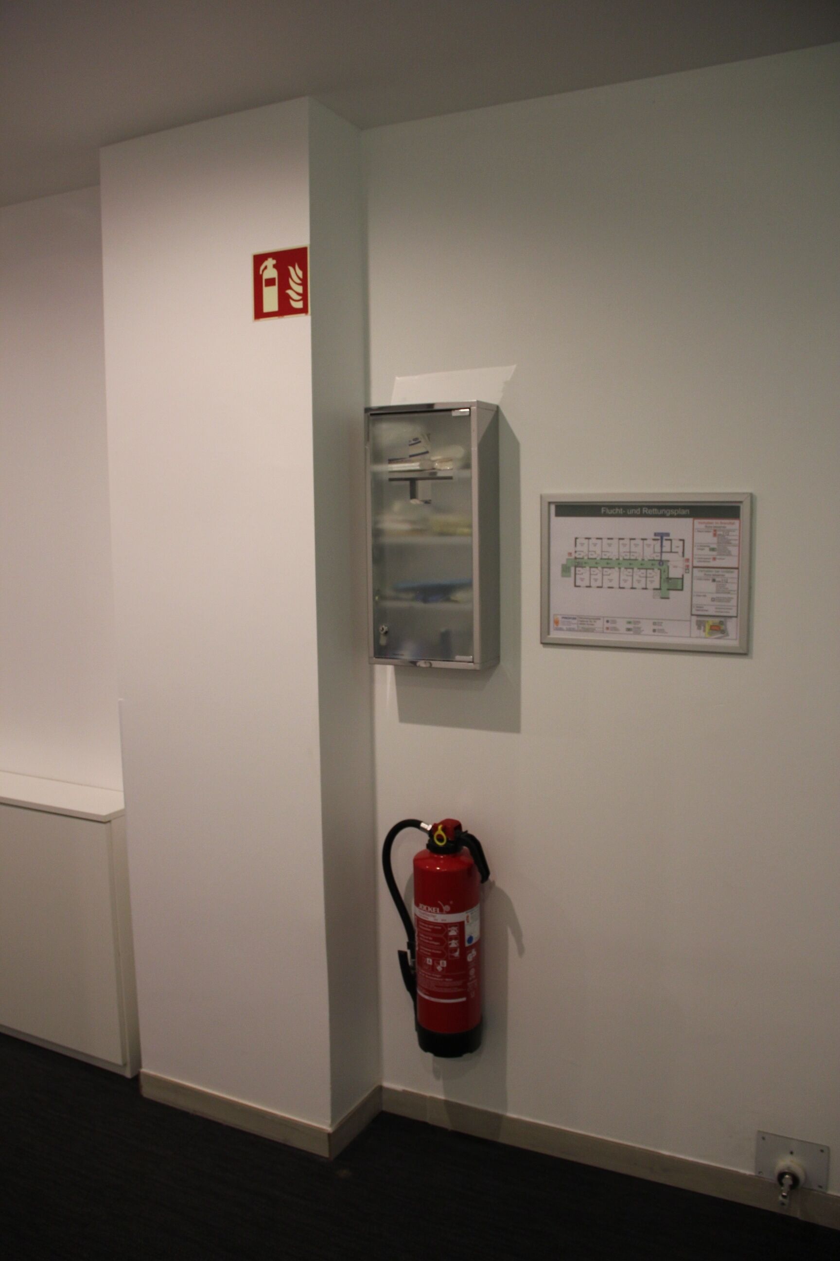 A hallway with a fire extinguisher mounted on the wall, a fire alarm, and a map of the building's layout.