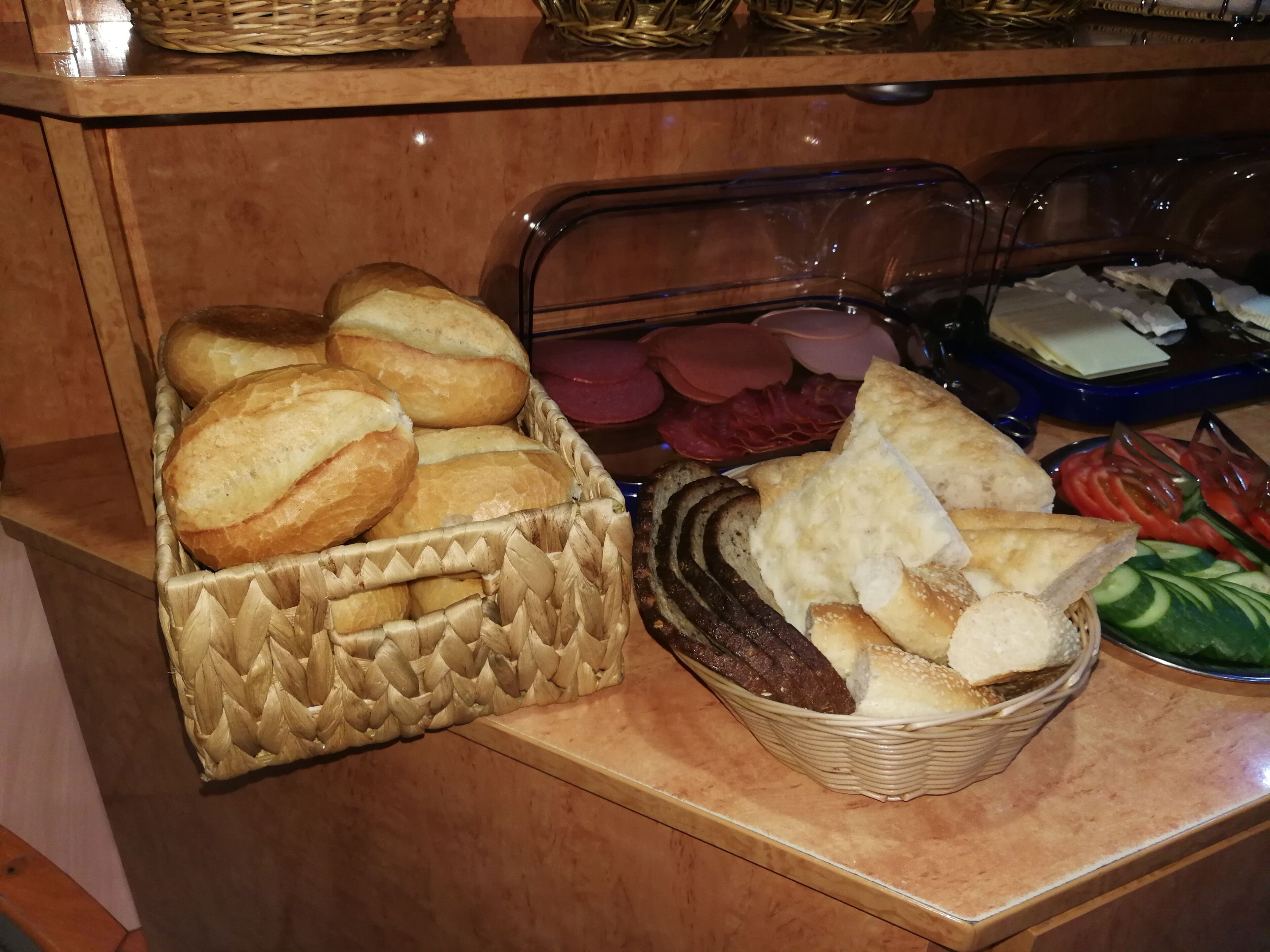 A buffet table with various breads, sliced meats, and fresh vegetables.