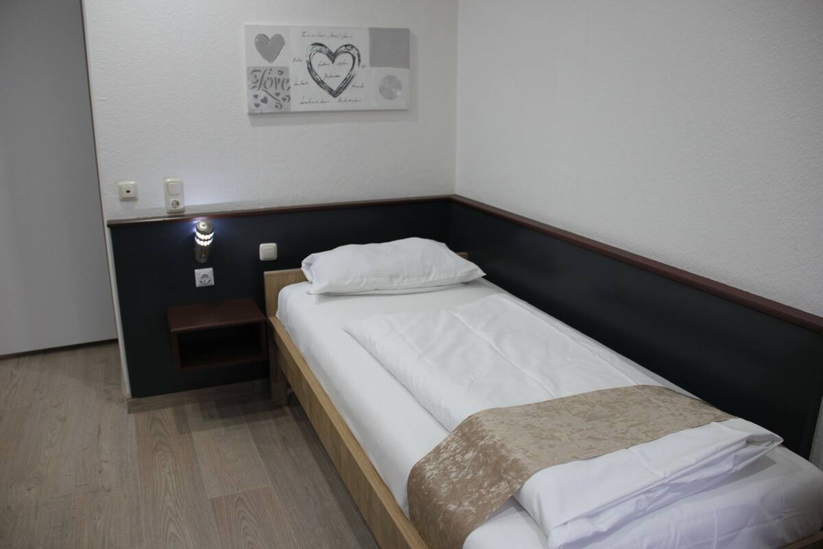 A single bed with a wooden headboard, a bedside table, and a wall-mounted light.