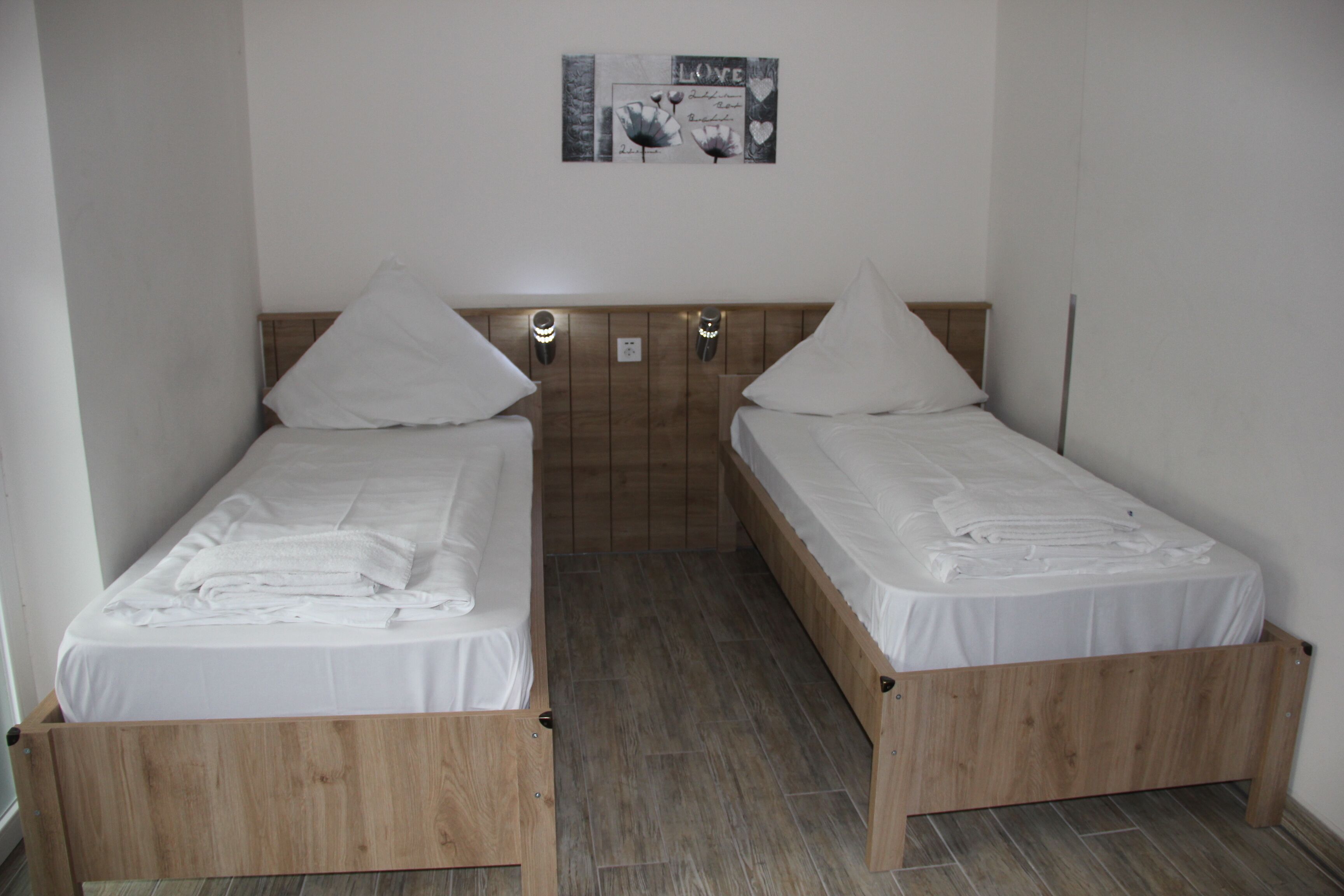 Une chambre double avec deux lits simples, des têtes de lit en bois, du linge de lit blanc et un tableau accroché au mur.