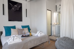 Una habitación de hotel moderna con una cama bien hecha, una ducha de vidrio y vista al baño.