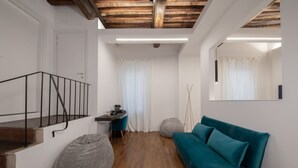 A modern living room with a wooden staircase, a teal sofa, a desk, and a large mirror on the wall. - Argentina Suites (Rome)