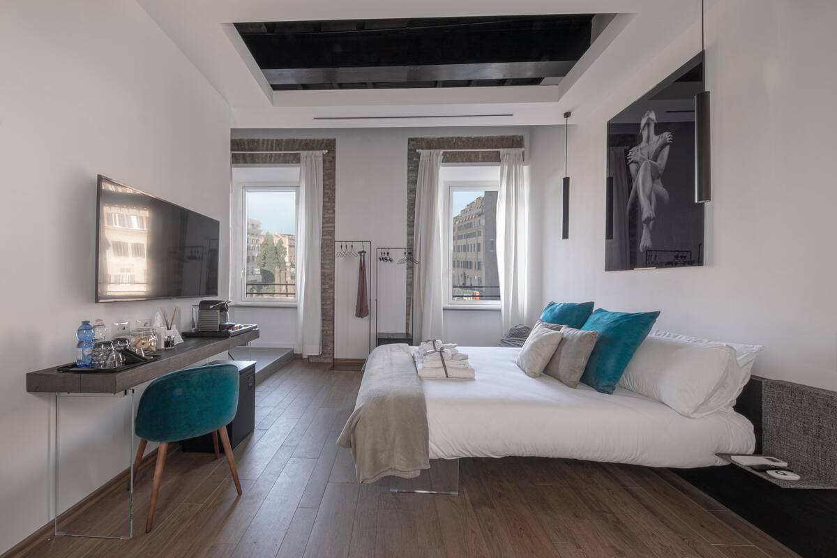 A modern hotel room with a bed, a desk, a chair, and a TV.