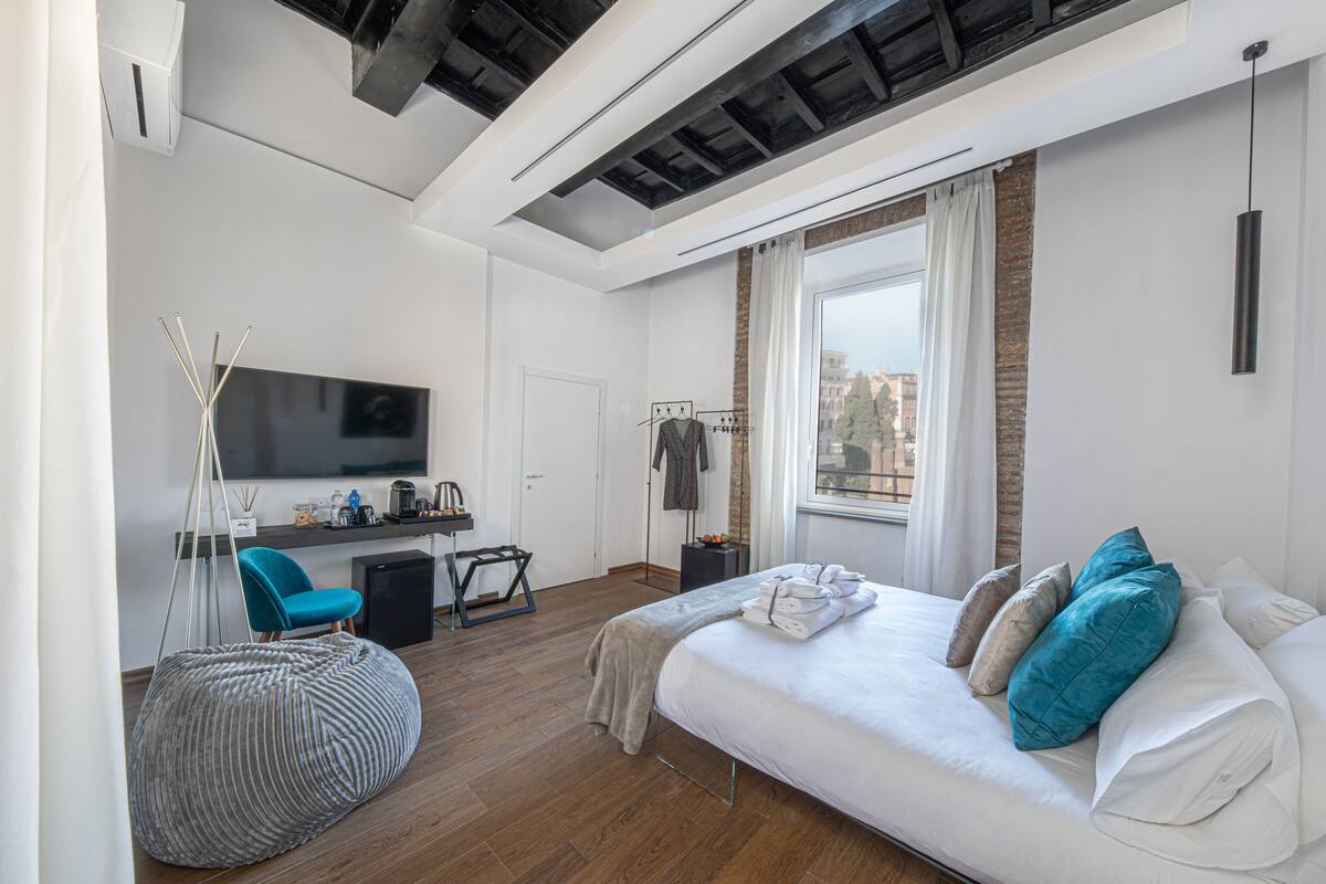 A modern bedroom with a bed, a desk, a chair, and a large window.