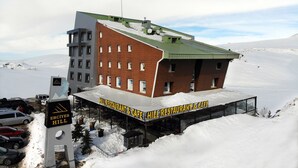 Een hotel met uitzicht op een skipiste, een overdekt terras en een bordje met 'HILL RESTAURANT & CAFE'.