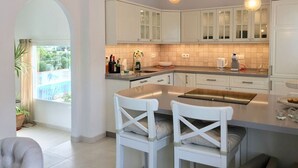 Een moderne keuken met witte kasten, een centraal eiland met barstoelen, en een uitzicht door een boog naar buiten.