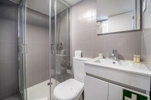 A modern bathroom with a glass shower enclosure, a white toilet, and a sink with toiletries. - Guadalupe Lofts (Braga)