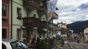 A street with buildings, a sign reading "Hoca Zait," and a motorcyclist on the road. - Locanda Alla Stella (Roana)