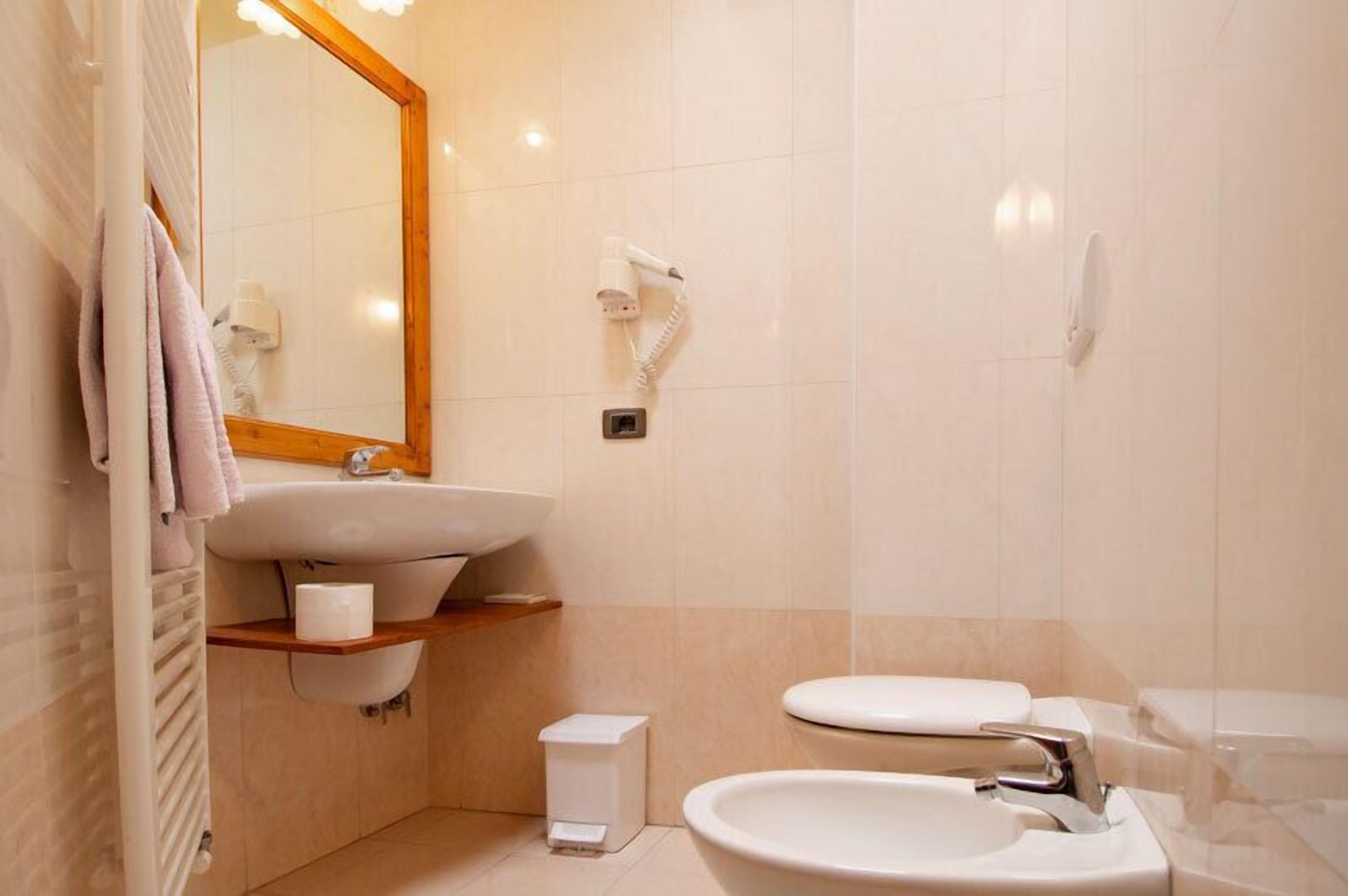 Une salle de bain moderne avec un grand miroir, un lavabo, des toilettes et un sèche-cheveux fixé au mur.