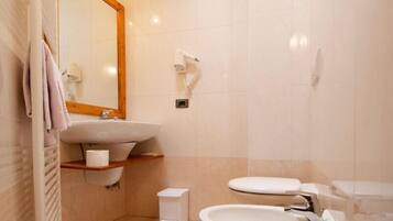 Une salle de bain moderne avec un grand miroir, un lavabo, des toilettes et un sèche-cheveux fixé au mur.