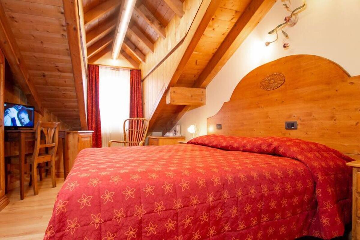 A wooden cabin room with a bed, a desk, a chair, and a television.