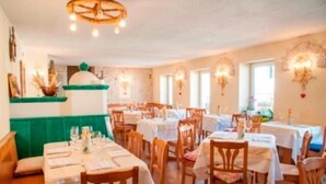 A restaurant with multiple tables and chairs, a green cushioned bench, and wall-mounted light fixtures. - Locanda Alla Stella (Roana)