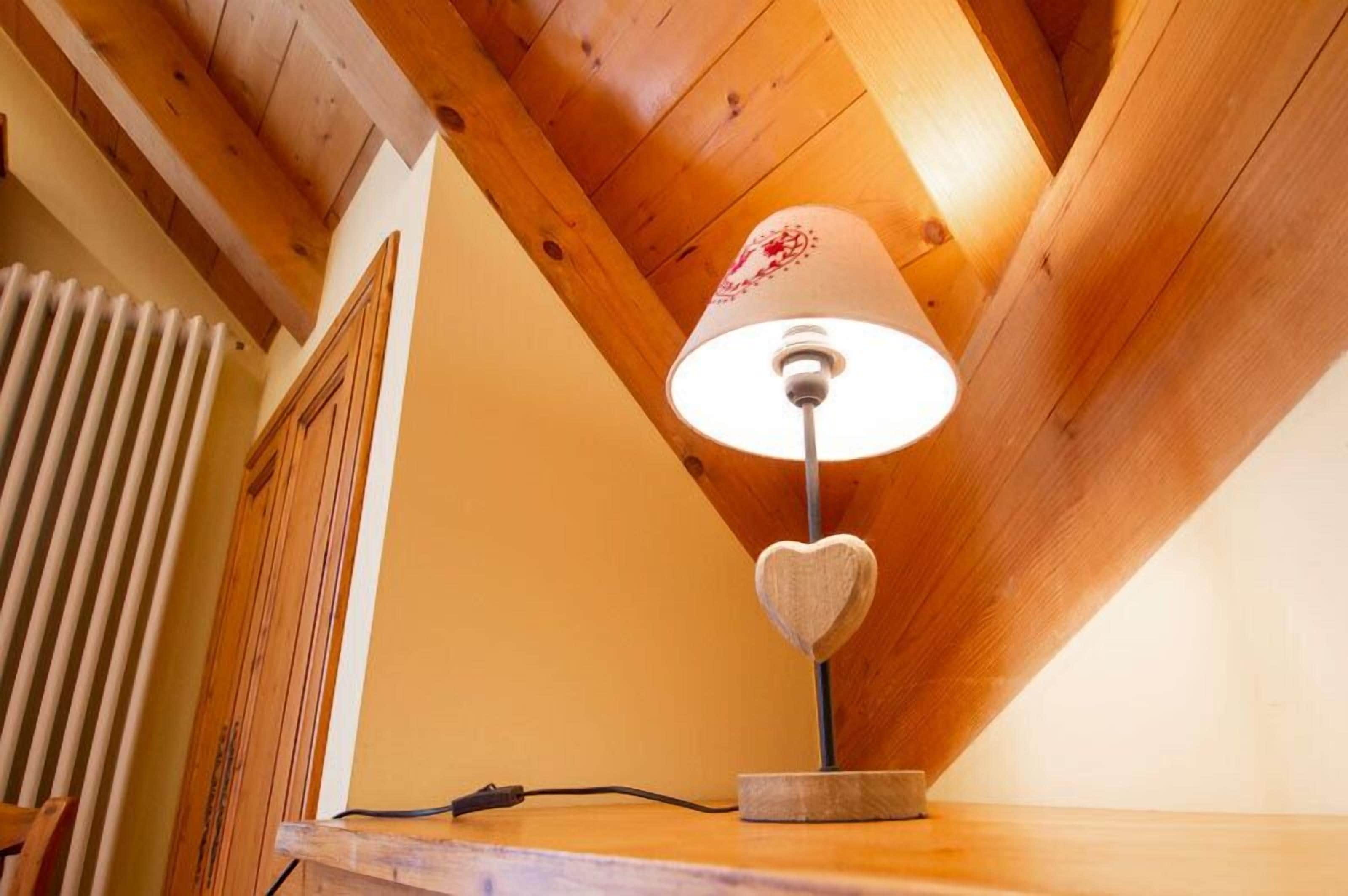 Un plafond en bois à pente douce, un radiateur blanc et une lampe de table dont le pied est en forme de cœur.