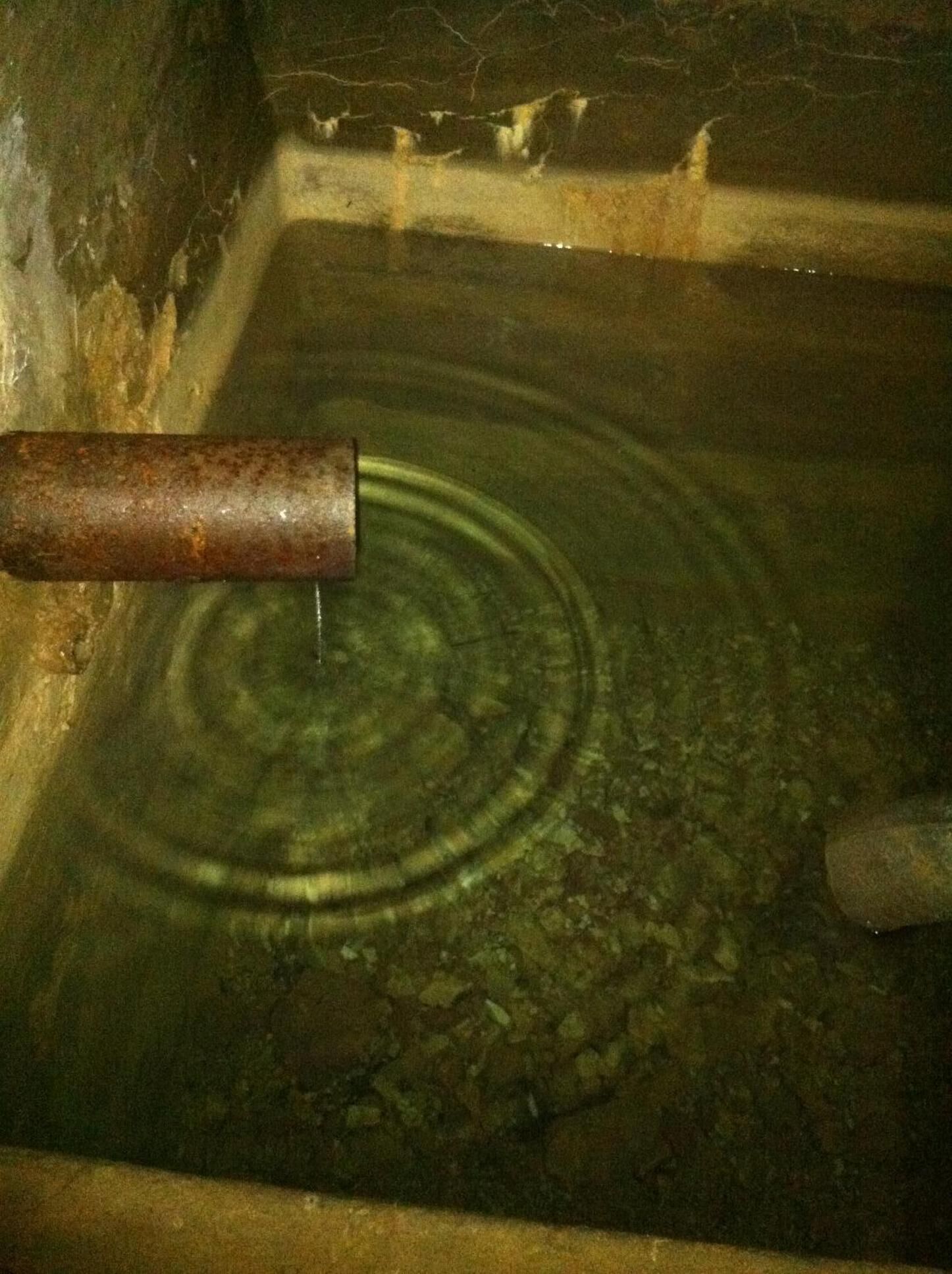 Un élément décoratif aquatique composé d’un tuyau rouillé dans un bassin en pierre.