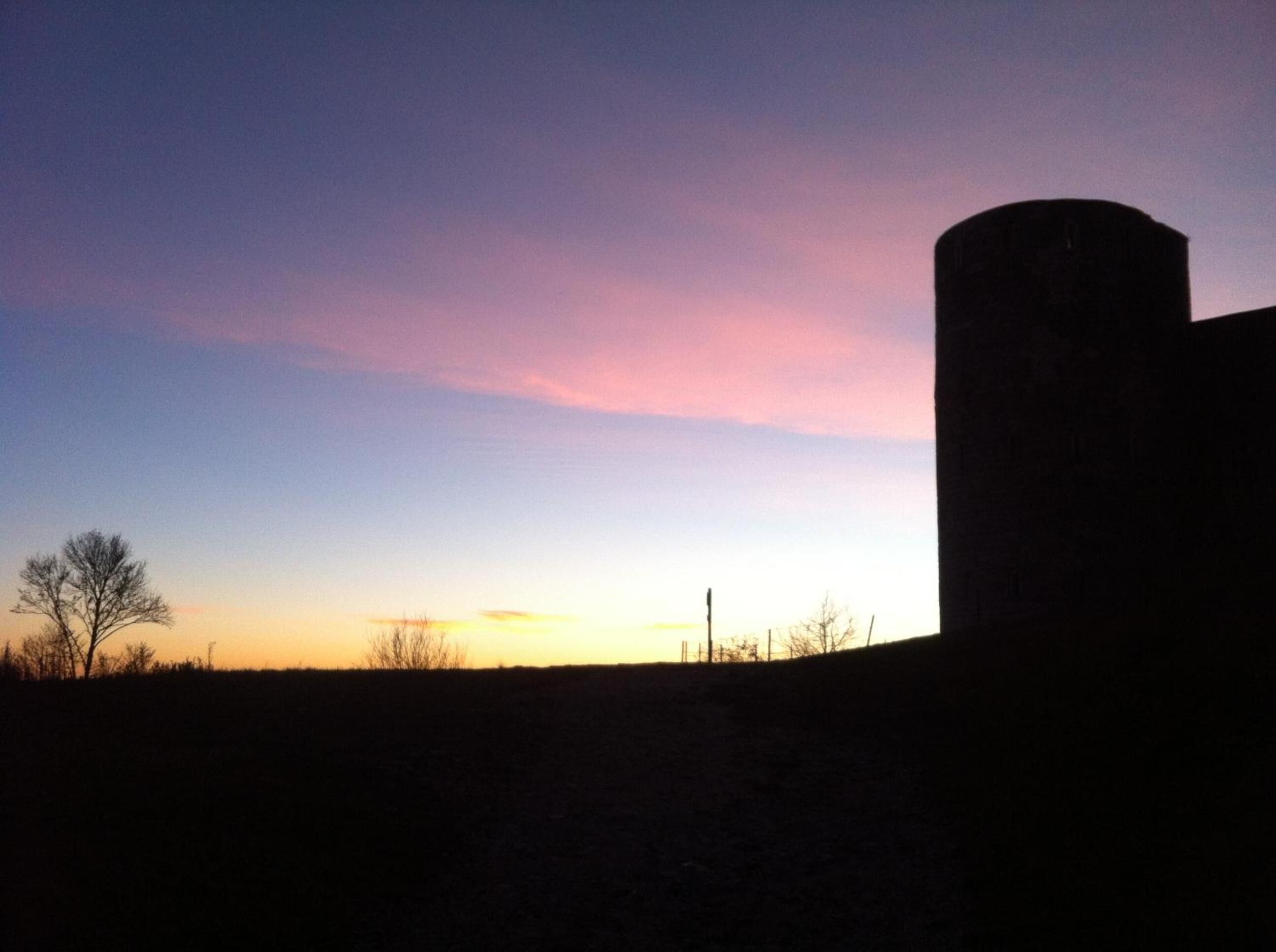Ein Sonnenuntergang mit der Silhouette eines Gebäudes und eines Baumes auf einem Hügel.