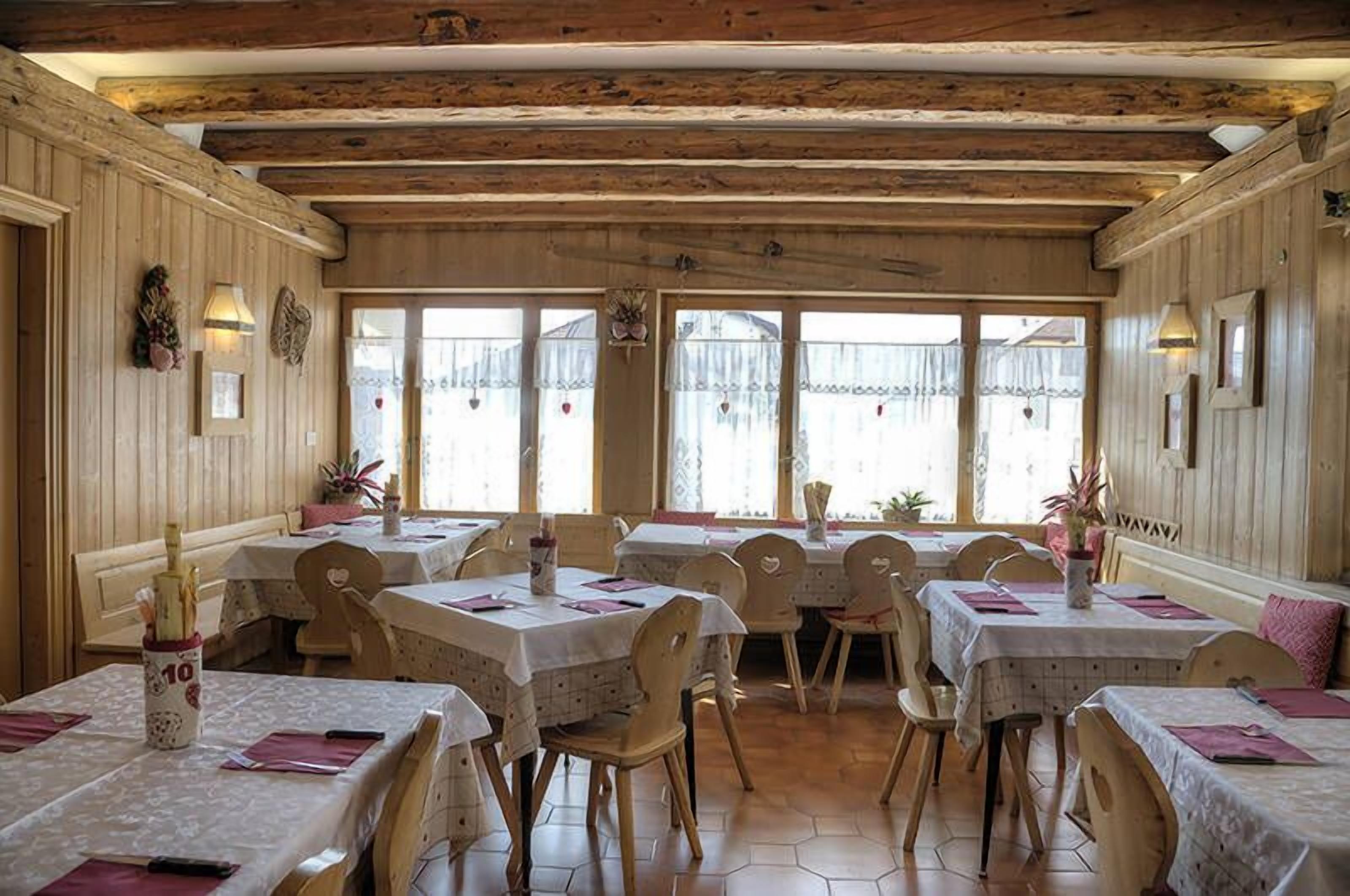 A restaurant with wooden beams, hexagonal tiled floor, and tables with white tablecloths and pink napkins.