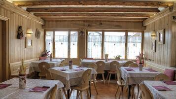 A restaurant with wooden beams, hexagonal tiled floor, and tables with white tablecloths and pink napkins.
