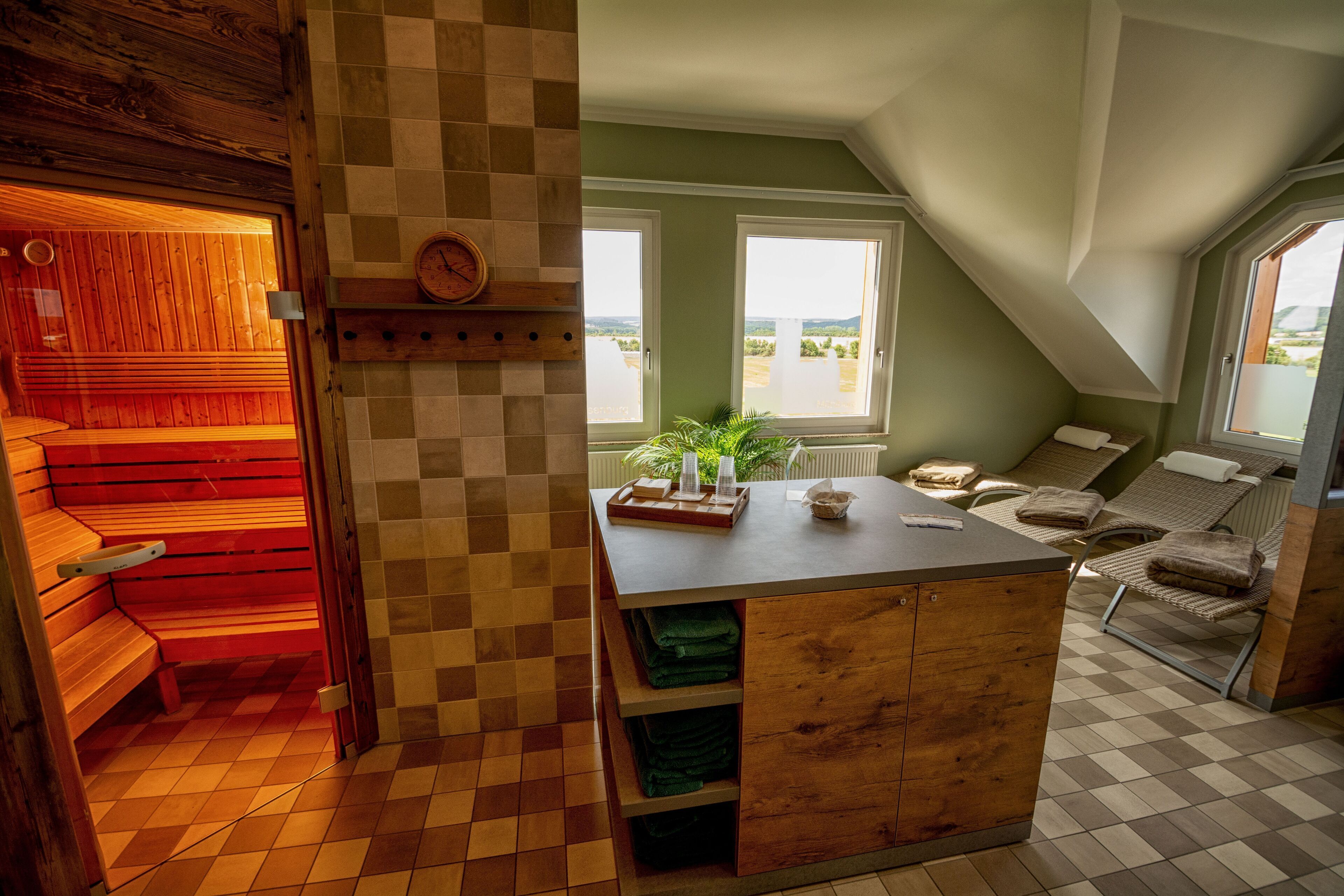 Ein Saunaraum mit Holzbänken, einem Holzkasten mit Handtüchern und Blick ins Freie durch ein Fenster.